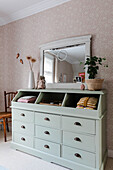 Mint green chest of drawers with mirror and decorations in floral wallpapered room