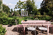 Garden table with white and pink chairs on a gravelled area in the summer garden