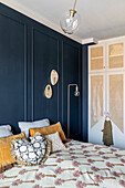 Bed with colourful cushions and floral bedspread in front of dark blue wall in bedroom