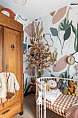 Baby room with wooden wardrobe, floral patterned wallpaper and decorative tree