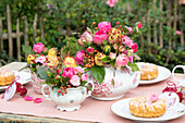 Tea set with bouquets of roses and pastries on garden table in summer