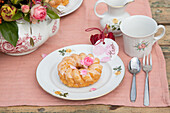 Gedeckter Tisch mit Porzellan und Kuchen auf rosa Tischdecke im Garten