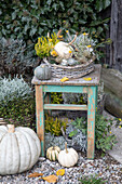 Autumnal pumpkin and flower arrangement on a rustic wooden stool in the garden