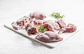 Portioned raw rabbit with rosemary on a white chopping board