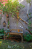 Bench, wooden table and fairy lights in front of a brick wall in an autumnal courtyard