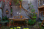 Autumnal courtyard with wooden table, fairy lights and climbing plants on brick wall