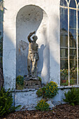 Steinfigur in Nische mit Farnen und Blütenstauden