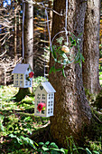 Cottage-shaped lanterns and floral wreath hanging from a tree in the forest