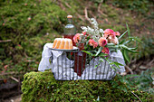 Picnic basket with liqueur, cake and flowers in the forest