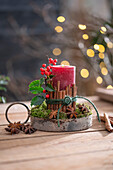 Candle on birch disc with cinnamon sticks wrapped with red winter berry, holly, star anise and moss, Advent arrangement