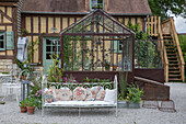 Glass greenhouse and wrought-iron bench with cushions in the country house garden