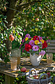 Sitzplatz unter Apfelbaum mit herbstlichen Strauß aus Dahlien (Dahlia), Knöterich (Persicaria), Borretsch und Korb mit Äpfeln