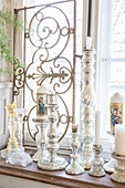 Silver candlesticks and decorated glass candle holders on a windowsill in front of a decorative grille