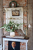 Vintage-Dekoration vor Backsteinwand mit Blumenstrauß und Madonnenstatue auf rustikalem Beistelltisch