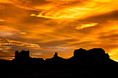 Colorful sunset skies over the Utah monuments in the Monument Valley Navajo Tribal Park in Utah & Arizona. L-R: Castle Butte & the Stagecoach, King on the Throne & Brigham's Tomb.