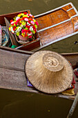 Ein traditioneller thailändischer Hut und Blumen, die auf Booten auf dem schwimmenden Markt von Damnoen Saduak in Thailand verkauft werden