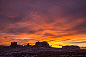 Farbenfroher Sonnenuntergang über den Monumenten von Utah im Monument Valley Navajo Tribal Park in Utah und Arizona. L-R: Castle Butte & die Postkutsche, König auf dem Thron & Brigham's Tomb