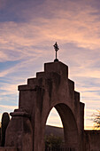 Ein gewölbtes Tor und ein Metallkreuz in der Mission San Xavier del Bac, Tucson, Arizona
