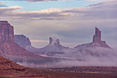 Foggy morning North Window view of the Utah monuments in the Monument Valley Navajo Tribal Park in Arizona. L-R: Setting Hen, Big Indian Chief.