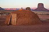 Das erste Licht des Tages auf dem Schornstein eines traditionellen Navajo-Hauses im Monument Valley Navajo Tribal Park in Arizona. Mitchell Butte liegt dahinter