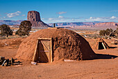Traditional Navajo hogan in front of Mitchell Butte in the Monument Valley Navajo Tribal Park in Arizona. A sweat lodge is a right.