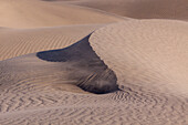 Sand blowing off the crest of a dune in the Mesquite Flat Sand Dunes in the Mojave Desert in Death Valley National Park, California.