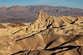Manly Beacon und erodierte Badlands der Furnace Creek Formation am Zabriskie Point im Death Valley National Park in Kalifornien. Das Badwater Basin und die Panamint Mountains sind dahinter zu sehen