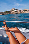 Legs of a young tanned woman, relaxed on a boat in Ibiza, with the castle and city walls in view