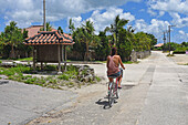 Young woman rides bike in Taketomi Island, Okinawa Prefecture, Japan