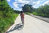 Junge Frau fährt Fahrrad auf der Insel Taketomi, Präfektur Okinawa, Japan