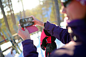 Junge attraktive Frau beim Fotografieren mit dem Mobiltelefon im Skigebiet Pyha, Lappland