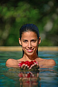 Young attractive woman holding red flowers in an infinity edge swimming pool. The Dutch House, Galle, Sri Lanka