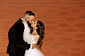 Bride and groom kissing against brick wall