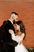 Bride and groom embracing against brick wall