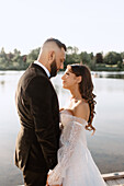 Bride and groom standing face to face on lakeshore