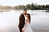 Groom kissing bride on lakeshore