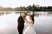 Bräutigam küsst die Hand der Braut am Seeufer