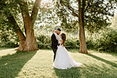 Bride and groom embracing in park