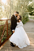 Braut und Bräutigam küssen sich auf einer Fußgängerbrücke im Park