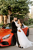 Brie and groom embracing at red car
