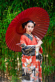 Porträt einer Frau in Kimono und mit Sonnenschirm im Park