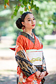 Nachdenkliche Frau in Kimono, stehend im Park