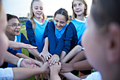 UK, Female soccer team members (10-11, 12-13) stacking hands in field