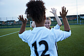 UK, Female soccer team members (10-11, 12-13) giving high five in field