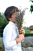 Junge (8-9) riecht an frisch gepflücktem Lavendel auf einem Feld