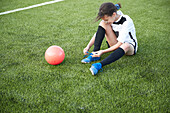 UK, Female soccer player (10-11) tying shoe in field