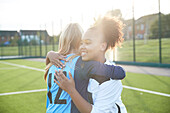 UK, Lächelnde weibliche Fußballspielerinnen (12-13), die sich auf einem Feld umarmen