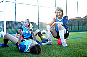 UK, Playful female soccer players (10-11, 12-13) relaxing in field