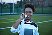 UK, Portrait of female soccer player (12-13) showing gold medal in field