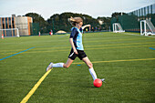 UK, Weibliches Mitglied einer Fußballmannschaft (10-11) kickt Ball auf einem Feld